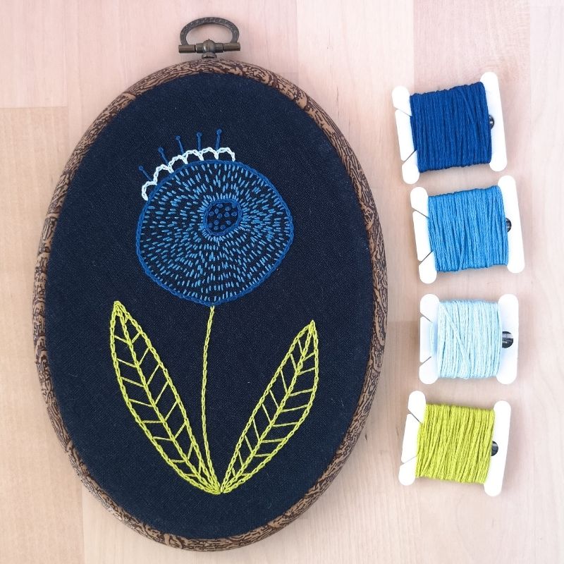 Broderie de fleurs modernes bleues sur tissu foncé dans un cerceau ovale